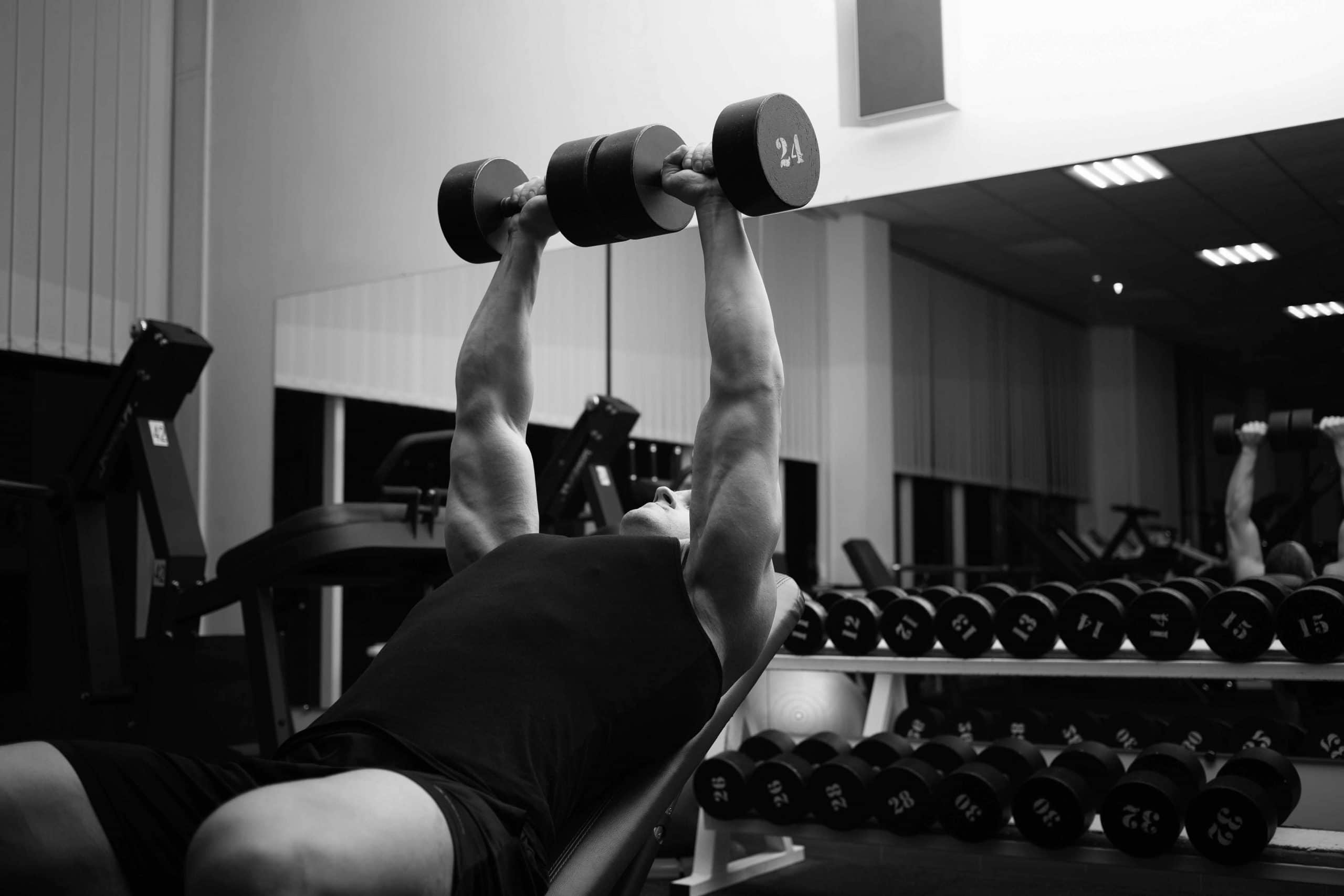 man-performs-an-exercise-with-dumbbells-on-a-simul-2021-10-21-02-41-19-utc-scaled.jpg